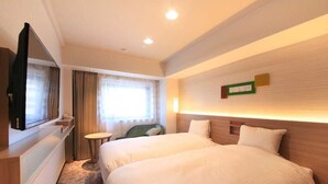 Quarto de hotel com duas camas, televisão, uma pequena mesa e janela com cortinas.