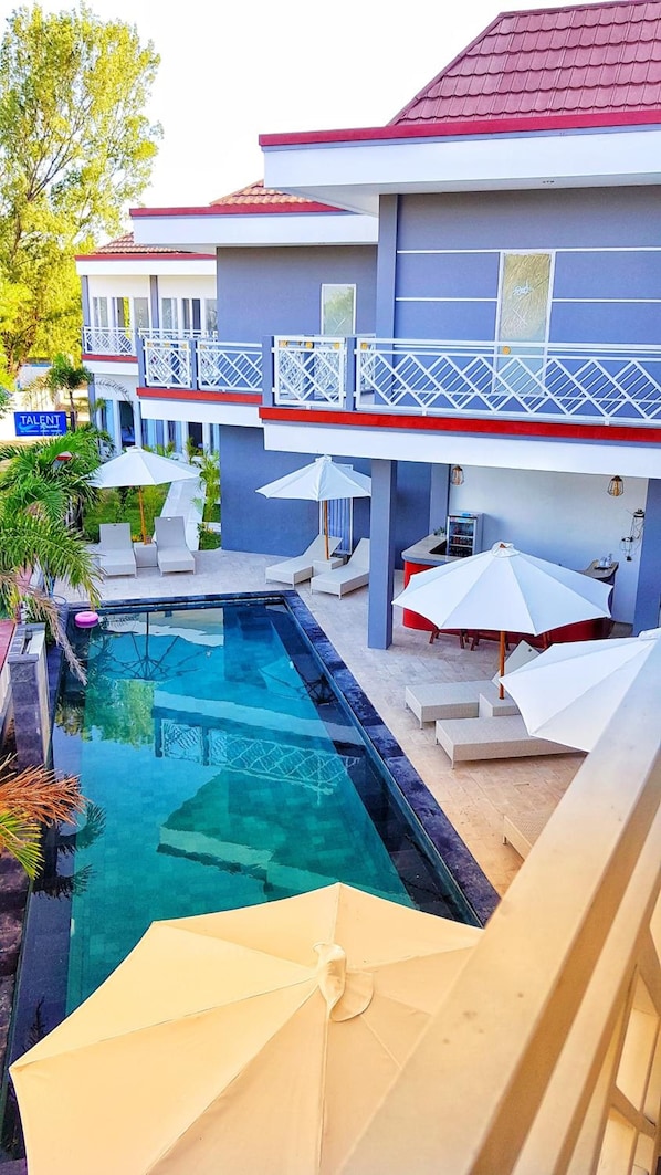 A hotel with a swimming pool, outdoor seating, and a balcony with railings.