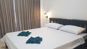 A neatly made bed with white sheets and two blue towels, a dark headboard, and a wall-mounted light fixture. - Talent Resort (Gili Trawangan)