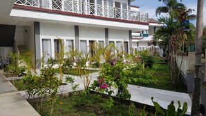 A hotel with a white exterior, multiple balconies with white railings, and a garden area with various plants and flowers. - Talent Resort (Gili Trawangan)