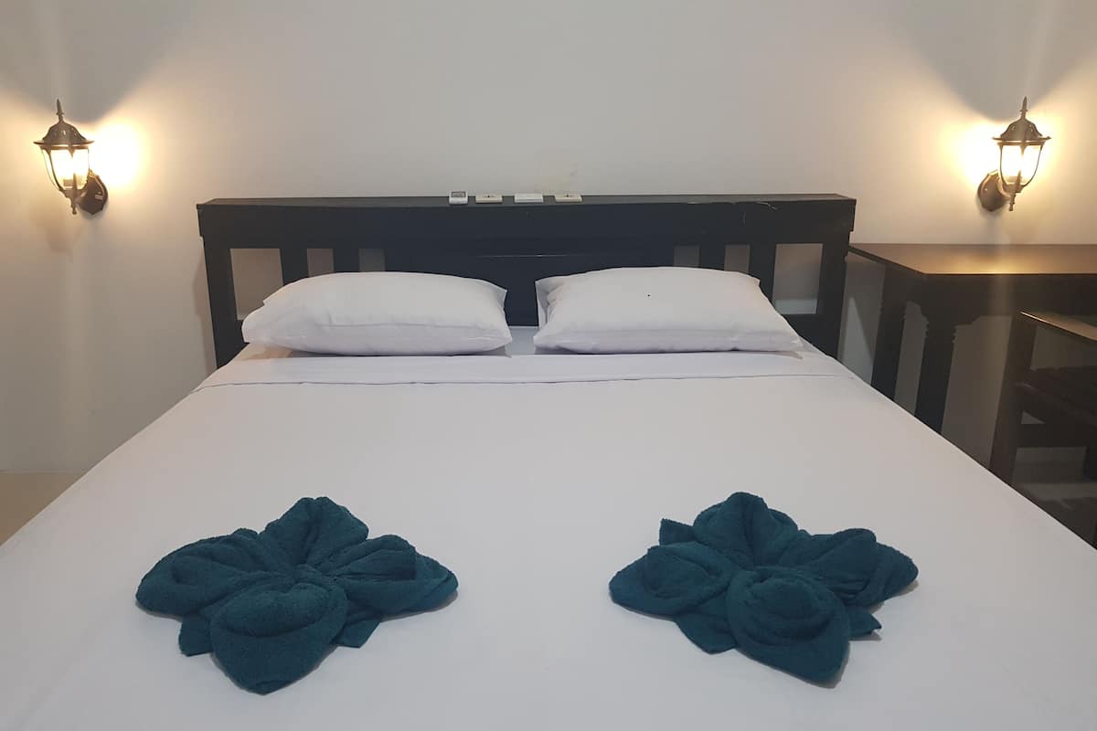 Un lit avec du linge de lit blanc, deux oreillers blancs et deux serviettes pliées posées sur le lit.