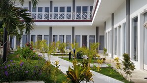 A modern building with a covered outdoor area featuring a pathway, potted plants, and a balcony with railings. - Talent Resort (Gili Trawangan)