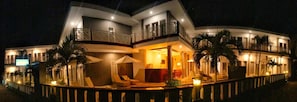 A multi-story hotel with a balcony on the second floor, outdoor seating area, and a well-lit entrance.