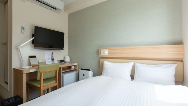 A hotel room with a bed, a desk with a chair, a television, and a small refrigerator. - fico HIJI (Hiji)