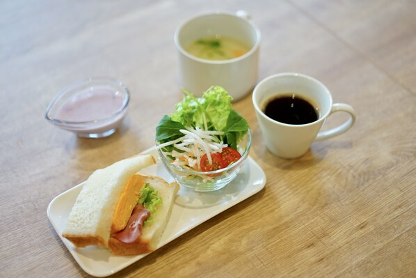 A sandwich on a white plate, a bowl of salad, a cup of tea, and a small dish of sauce on a wooden table. - fico HIJI (Hiji)
