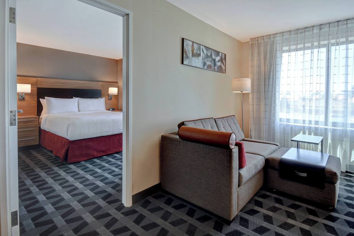 A hotel room with a bed, a sofa, a small table, and a lamp.