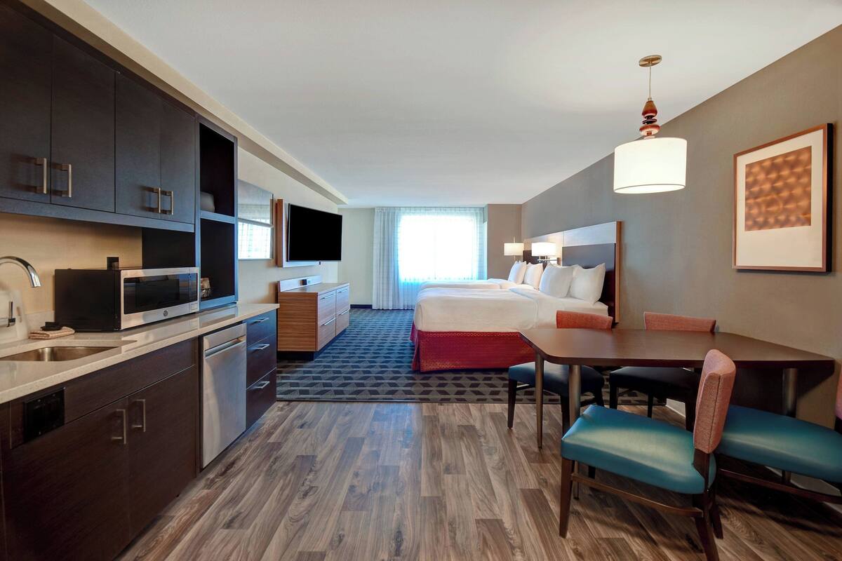 A hotel room with a bed, a desk, a chair, a television, a microwave, and a sink.