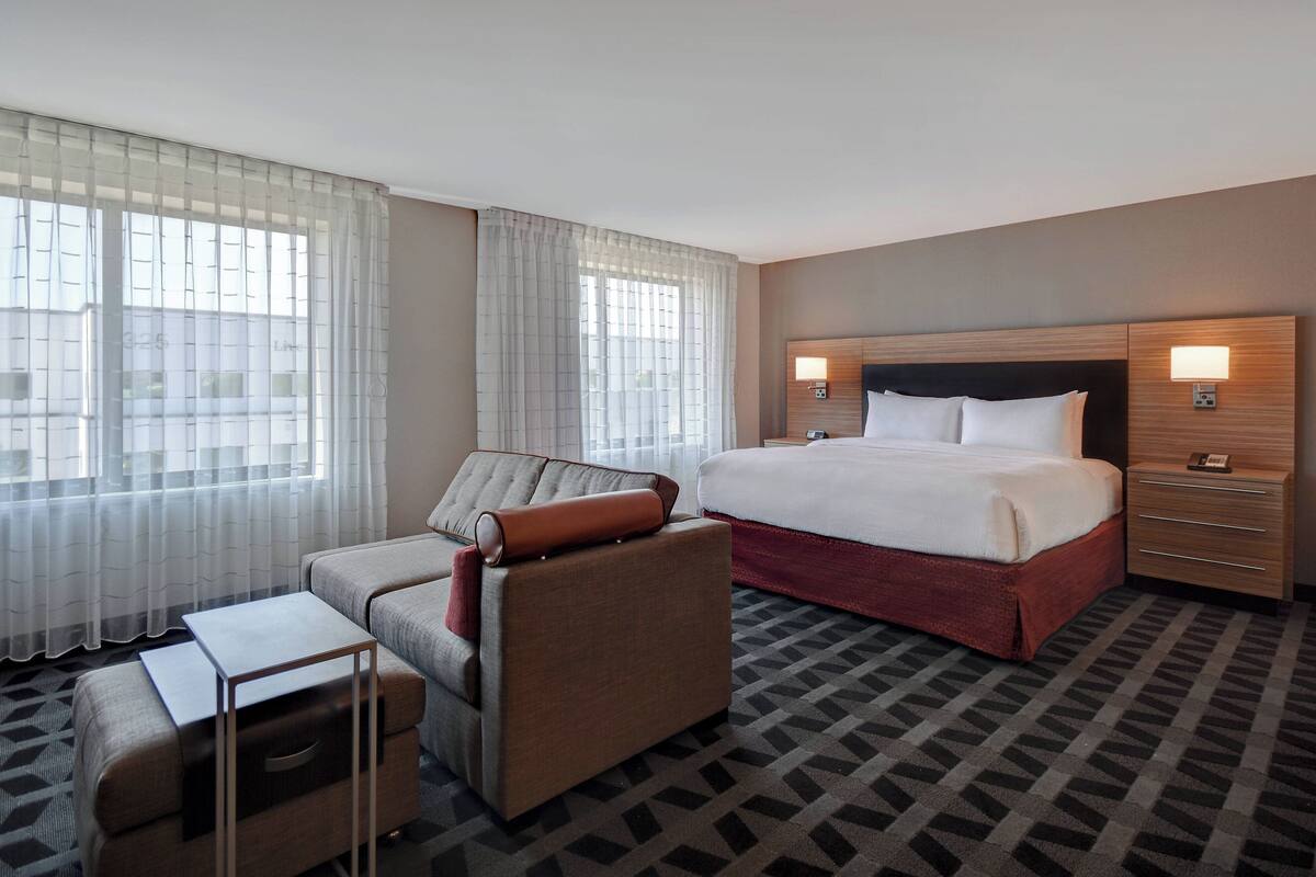 A hotel room with a large bed, a sofa, a desk, and a nightstand.