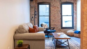 A cozy living room with a sofa, a coffee table, and a chair. There are two large windows with a view of the city. - Historic Downtown Loft  with King Bed and Wifi (Spokane)