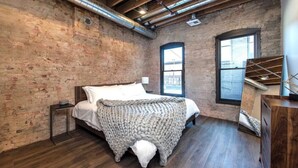 Ein Schlafzimmer mit freiliegenden Ziegelwänden, einer Holzbalkendecke und einem großen Fenster.