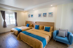 A hotel room with two beds, a blue armchair, and artwork on the wall. - Residence Lodge (Saipan)