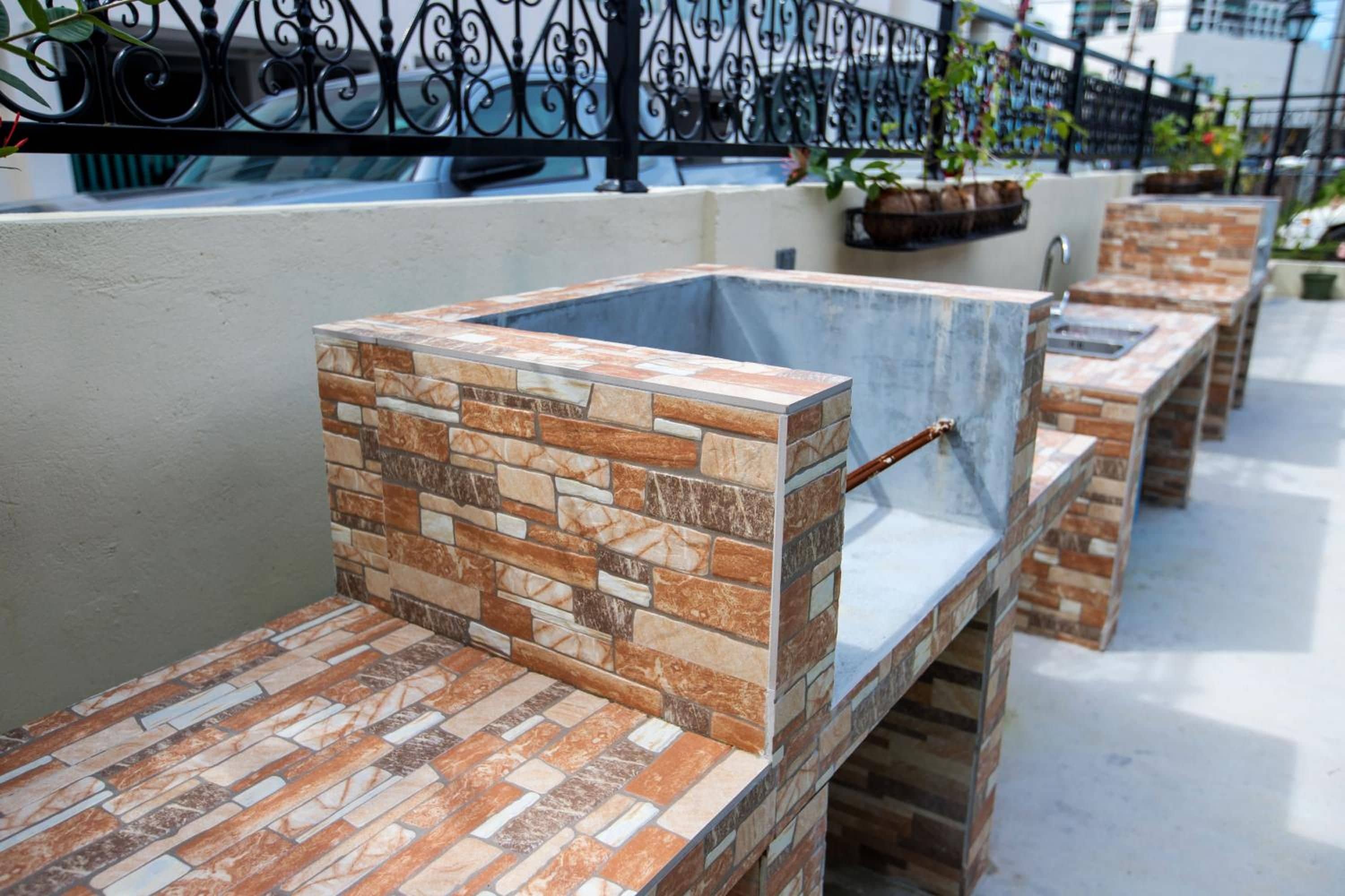 Espace extérieur aménagé avec des tables et des bancs à motifs de pierre, une clôture en métal et des plantes en pot.