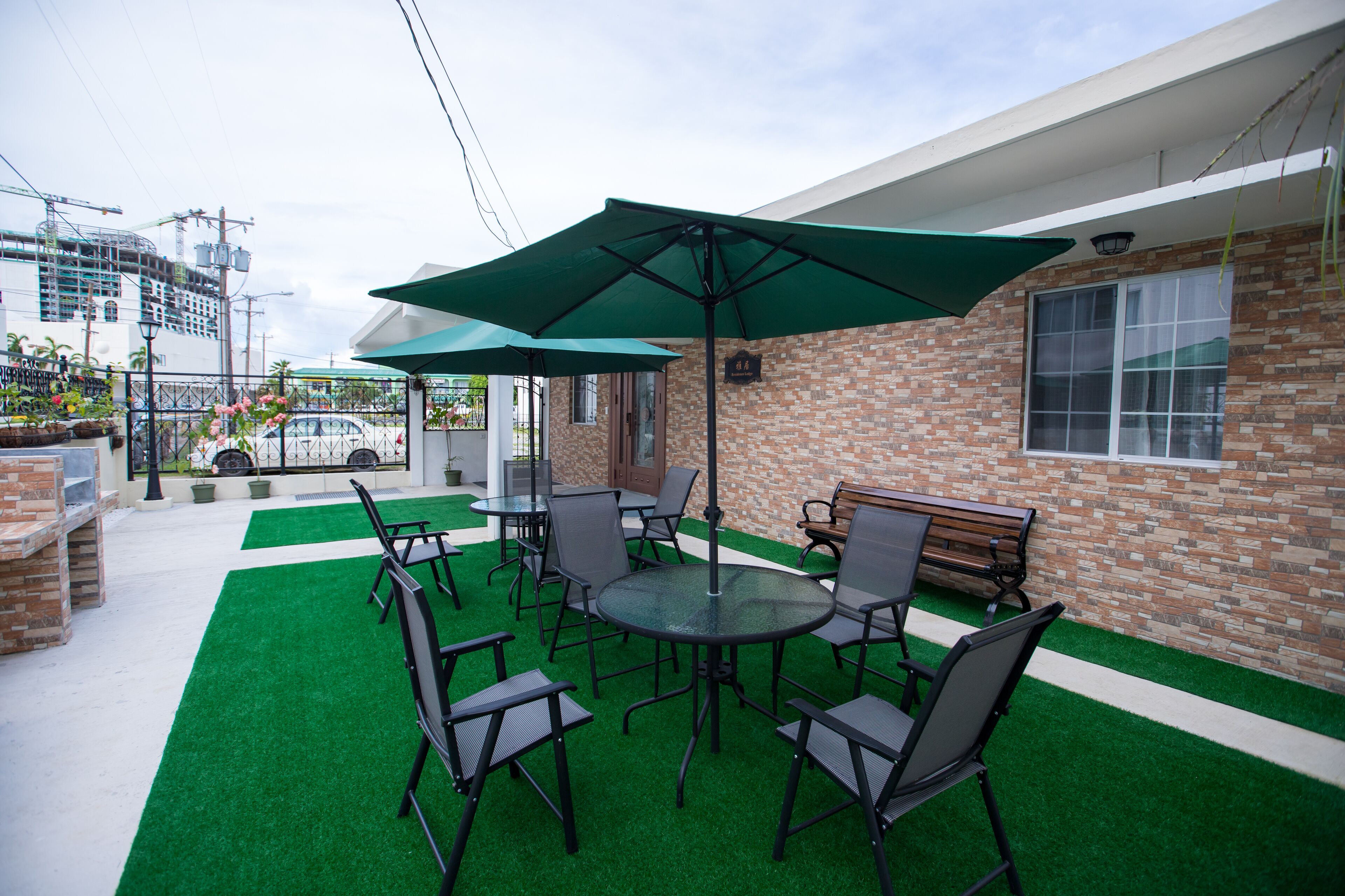 An outdoor patio with artificial grass, tables, chairs, and a large umbrella.