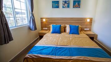 A hotel room with a large bed, two bedside tables, a window with curtains, and three wall-mounted paintings.