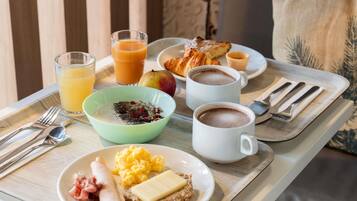 Un plateau de petit-déjeuner comprenant des œufs brouillés, du jambon, des toasts beurrés, un bol de céréales, deux tasses de café, un croissant et un verre de jus d’orange.