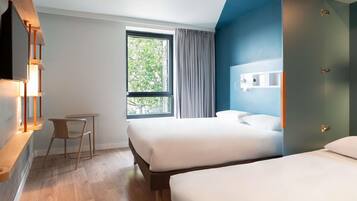 Habitación de hotel con dos camas, un escritorio, una ventana con cortinas y un televisor montado en la pared.