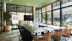 A modern indoor dining area with a large table, black and wicker chairs, a television, and a poster on the wall. - ibis budget Rouen Centre Rive Gauche (Rouen)