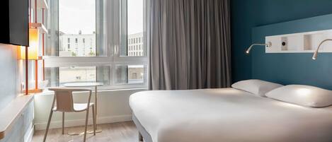 A modern hotel room with a bed, a desk, and a chair.