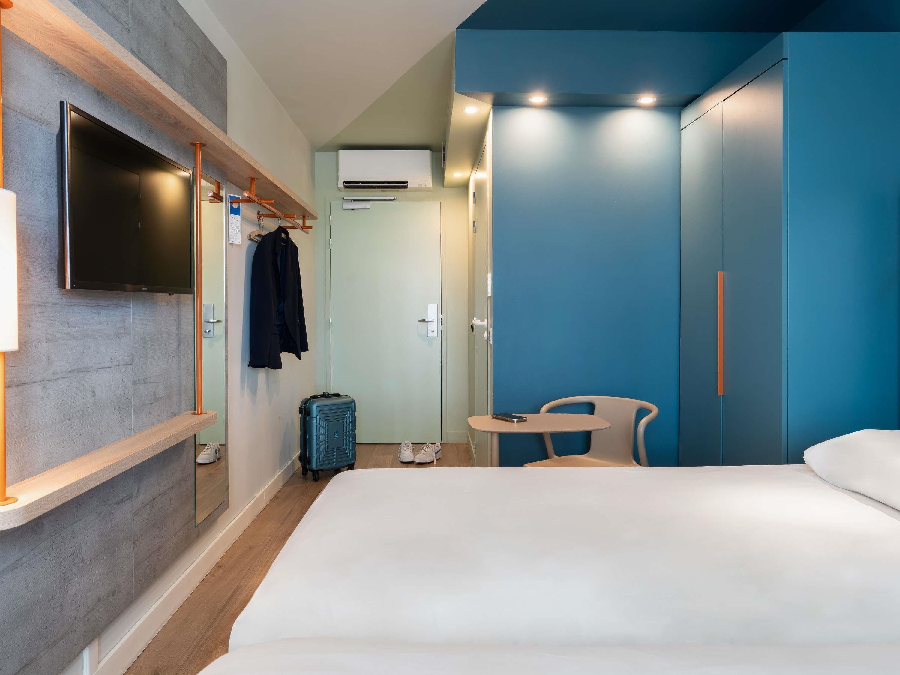 Een hotelkamer met een bed, een aan de muur bevestigde televisie, een bureau met stoel en een kledingkast.