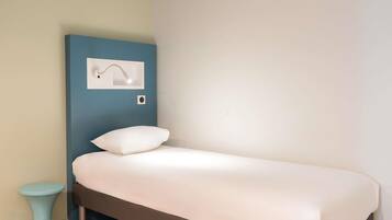 Una cama individual con colchón y almohada blancos, una mesita de noche azul y una lámpara de pared.