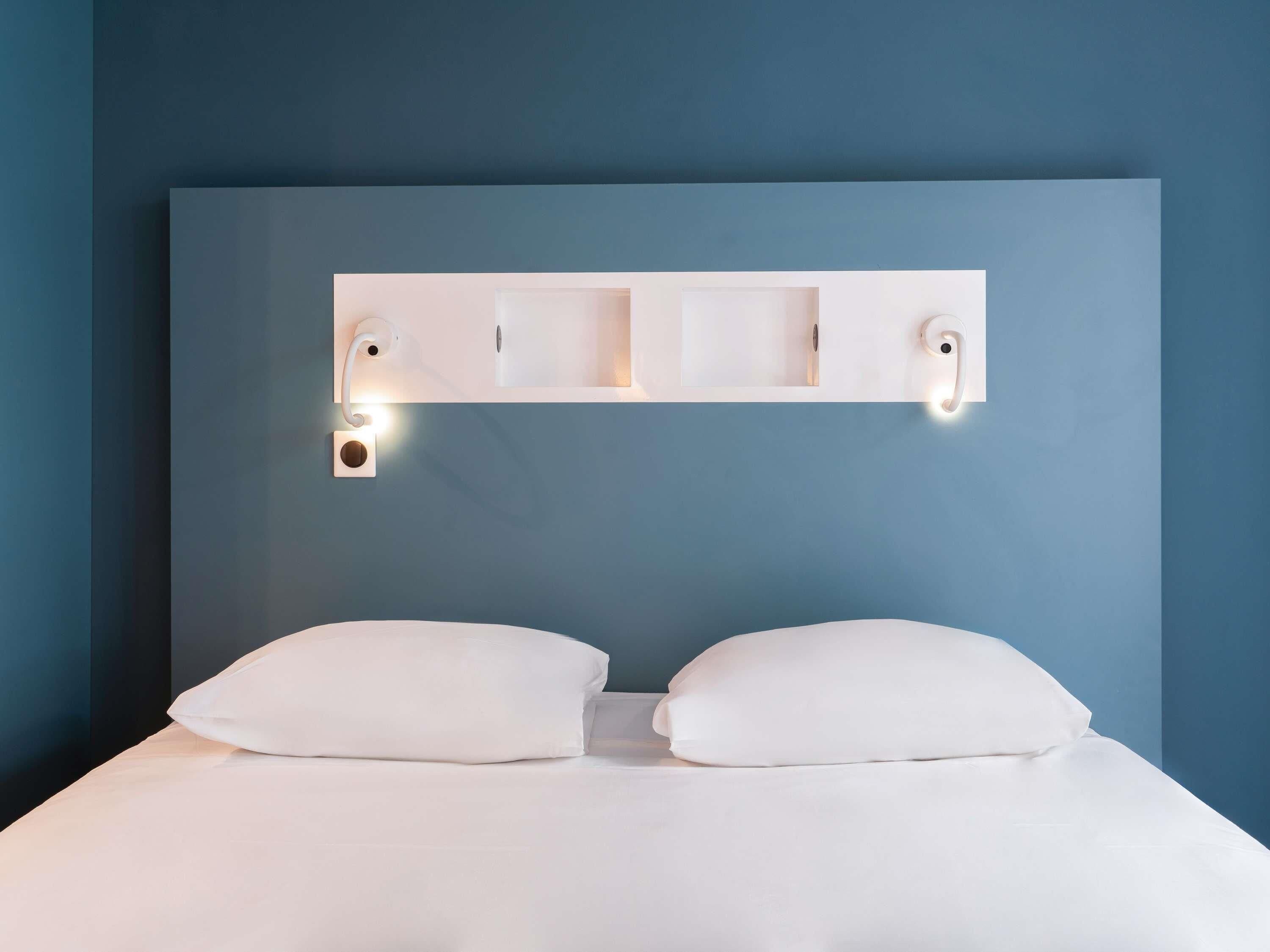 Un dormitorio con una cama grande, dos almohadas, cabecera con iluminación integrada y estante de pared.
