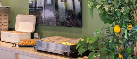 Montaje de bufé con calentador de alimentos, dispensador de bebidas y un amplio ventanal con vista a la vegetación.