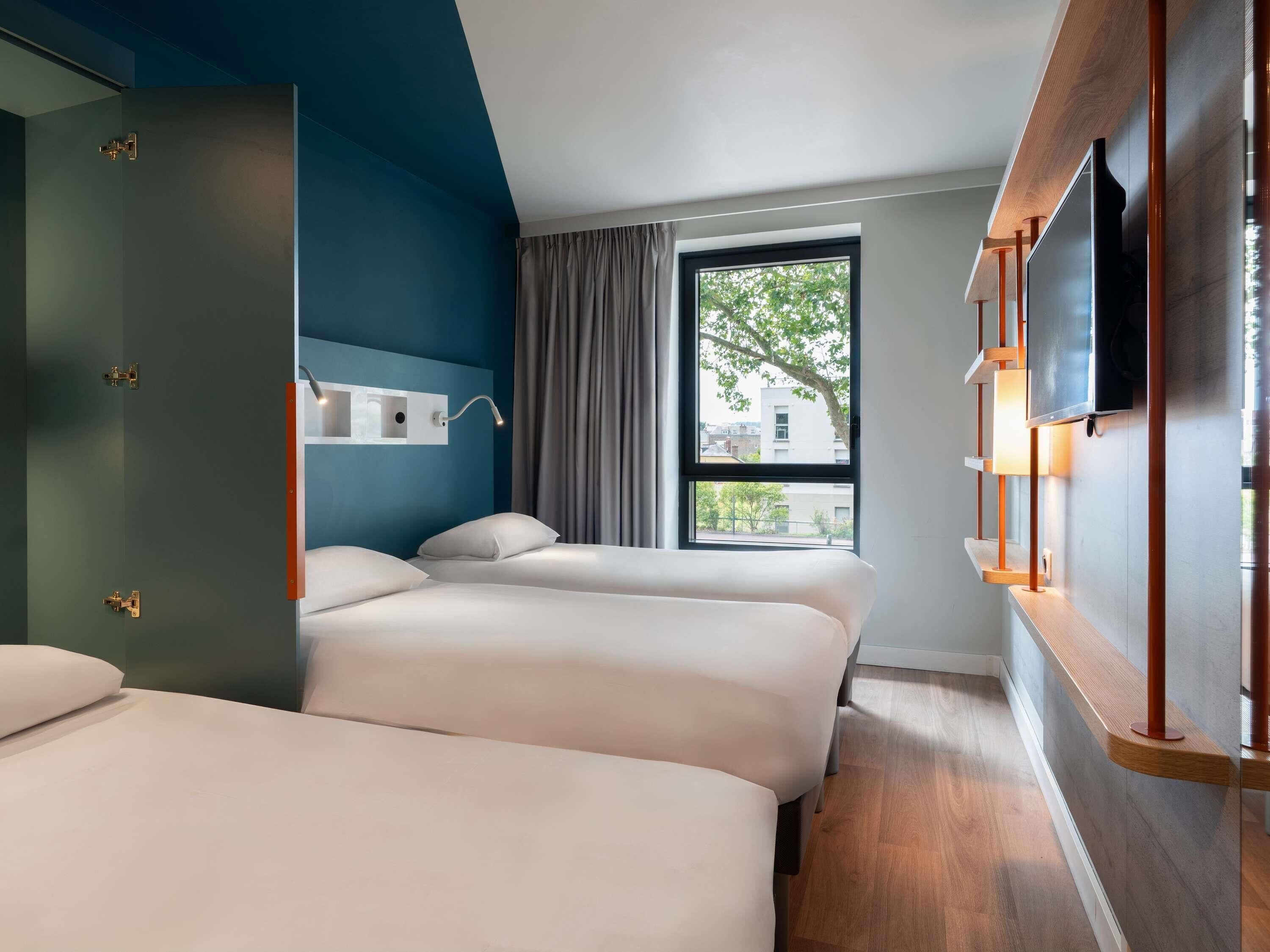 Une chambre d’hôtel avec deux lits, un téléviseur fixé au mur et une fenêtre donnant sur des immeubles.