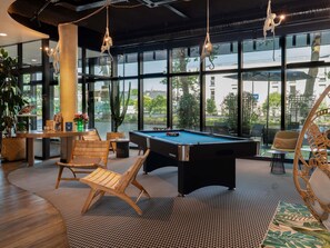 A pool table in a room with large windows, a pool table, and a lounge area with chairs.