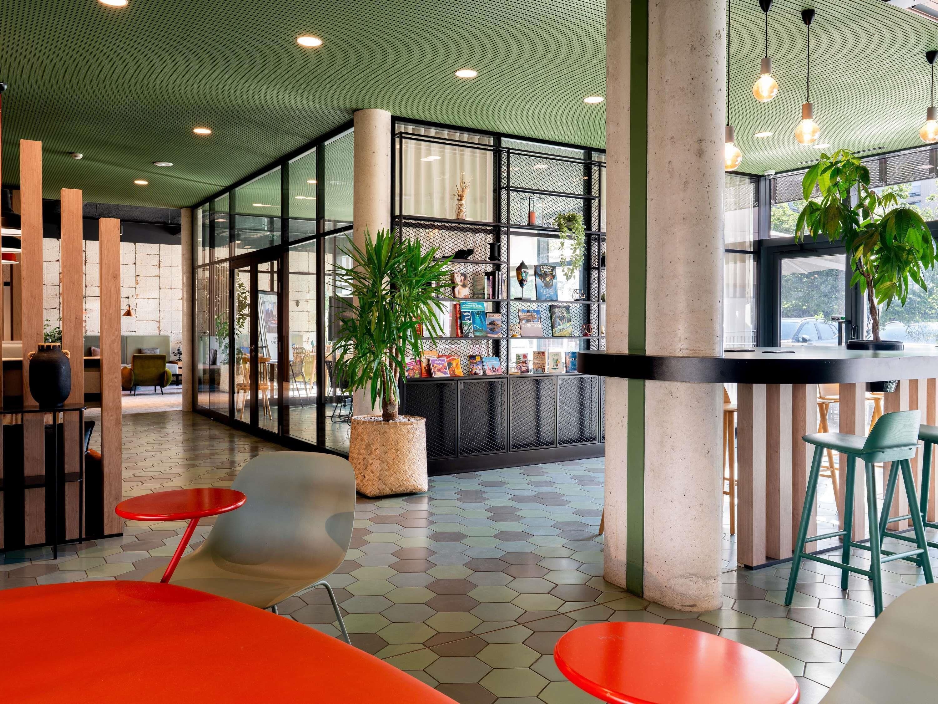 A modern interior with a hexagonal tiled floor, a central seating area with red and grey chairs, and a bookshelf with books and decorative items.