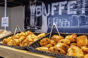 A display of assorted pastries in wicker baskets, with a backdrop featuring a chalkboard sign that reads "BUFFET." - ibis budget Rouen Centre Rive Gauche (Rouen)