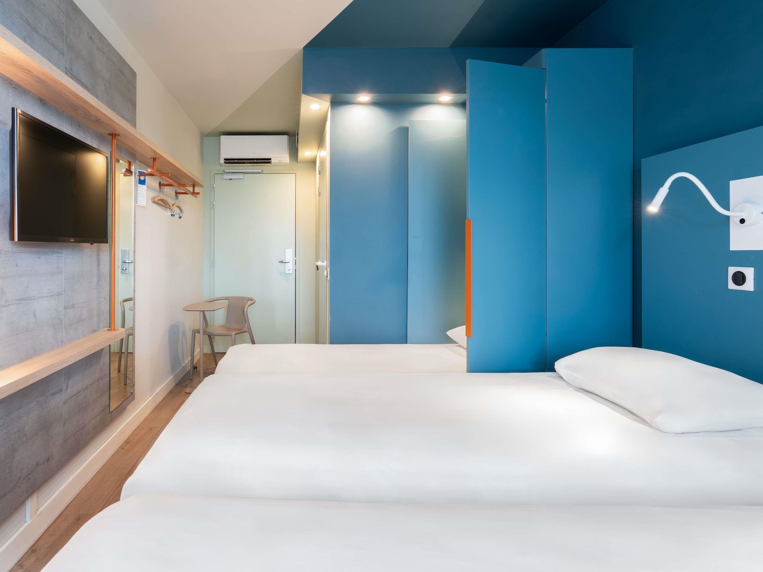 Une chambre d’hôtel moderne avec un grand lit, un téléviseur fixé au mur et une petite table avec une chaise.