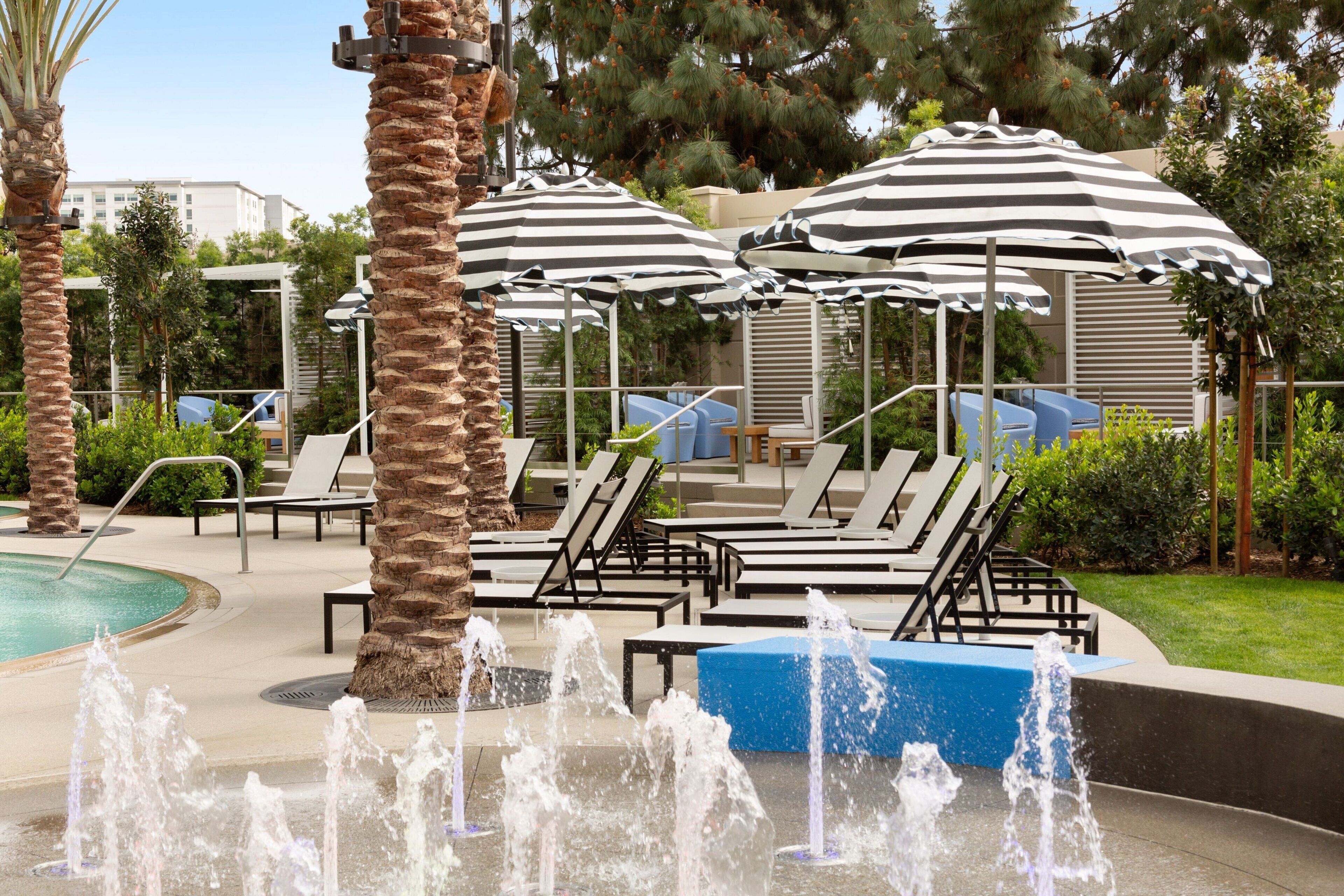 A pool area with multiple lounge chairs, striped umbrellas, and a water fountain.