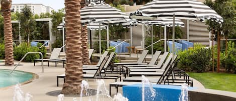 A pool area with multiple lounge chairs, striped umbrellas, and a water fountain.