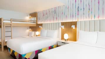 Habitación de hotel con dos camas, una litera, un corredor de cama con estampado geométrico y coloridos motivos, un aplique de pared y un cabecero de madera.