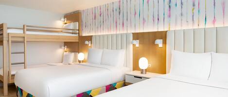 A hotel room with two beds, a bunk bed, a colorful geometric-patterned bed runner, a wall-mounted light fixture, and a wooden headboard.
