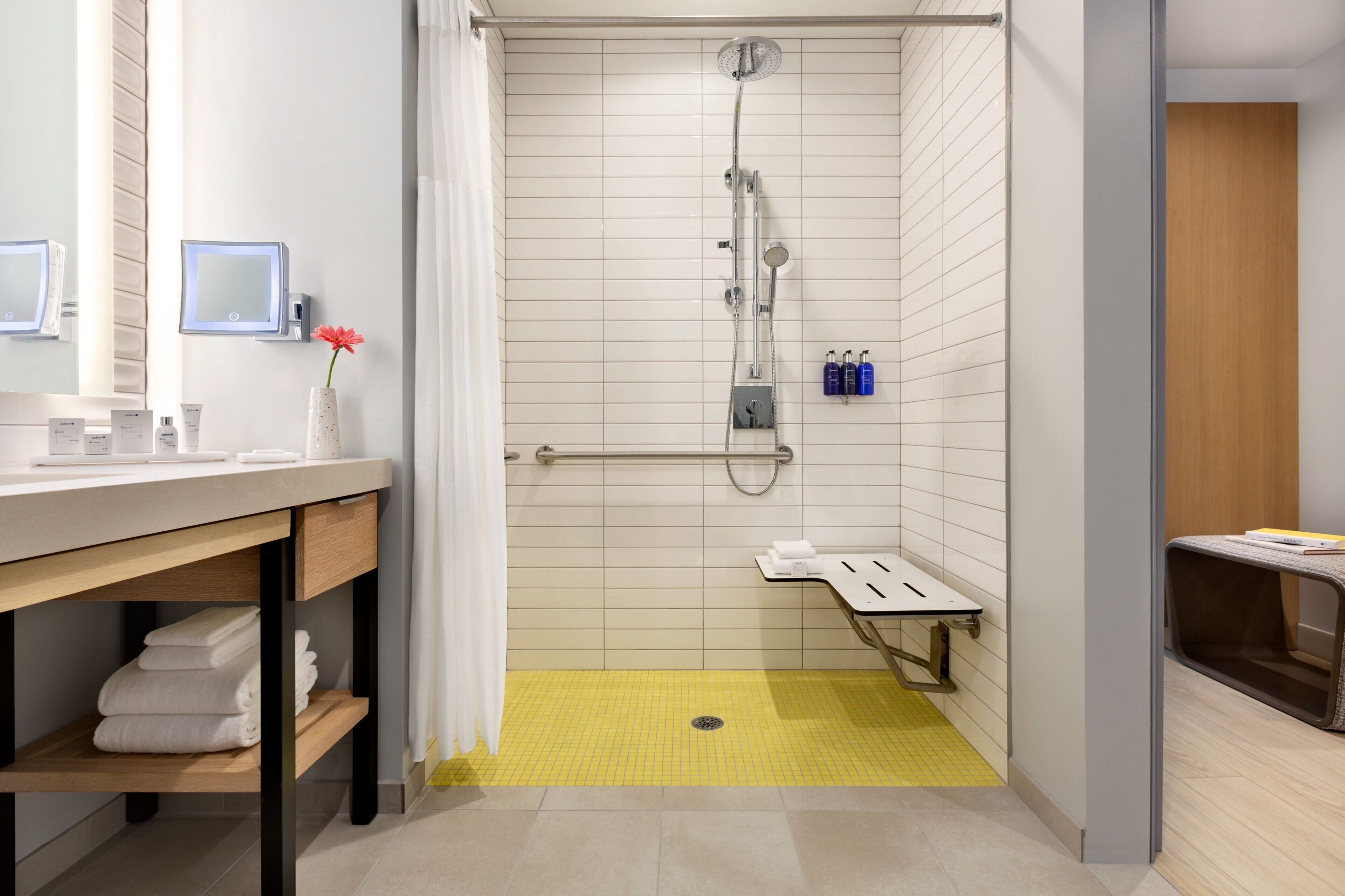 Ein modernes Badezimmer mit Dusche, Waschtisch mit Spiegel und einem kleinen Tisch mit Toilettenartikeln.