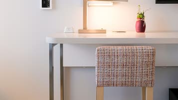 Un espace de travail moderne avec un bureau blanc, un tableau encadré, une petite plante en pot et une chaise avec un siège en osier.