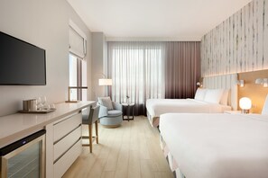 A modern hotel room with two beds, a desk with a flat-screen TV, a mini-fridge, a round chair, and a small table with a lamp. - The Viv Hotel, Anaheim, a Tribute Portfolio Hotel (Anaheim)