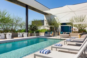 A modern outdoor pool area with lounge chairs, a swing chair, and a covered seating area. - The Viv Hotel, Anaheim, a Tribute Portfolio Hotel (Anaheim)