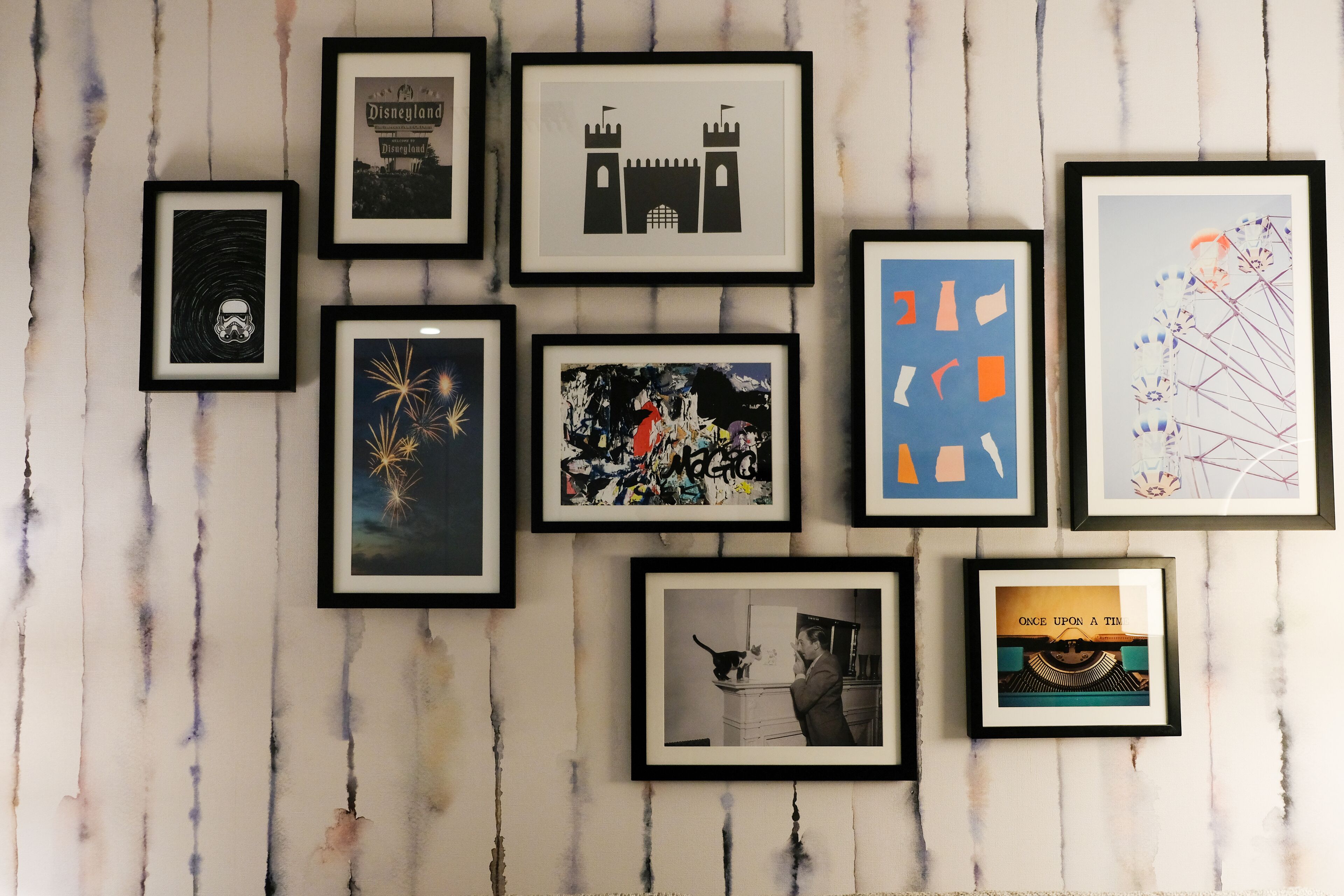 A wall with various framed artworks including a castle, fireworks, and abstract designs.