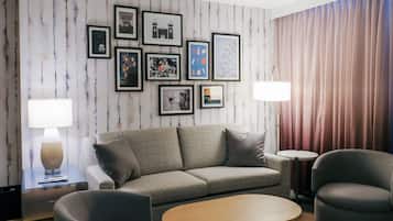 A modern living room with a grey sofa, a round coffee table, and two armchairs. There are framed pictures on the wall and a lamp on a side table.