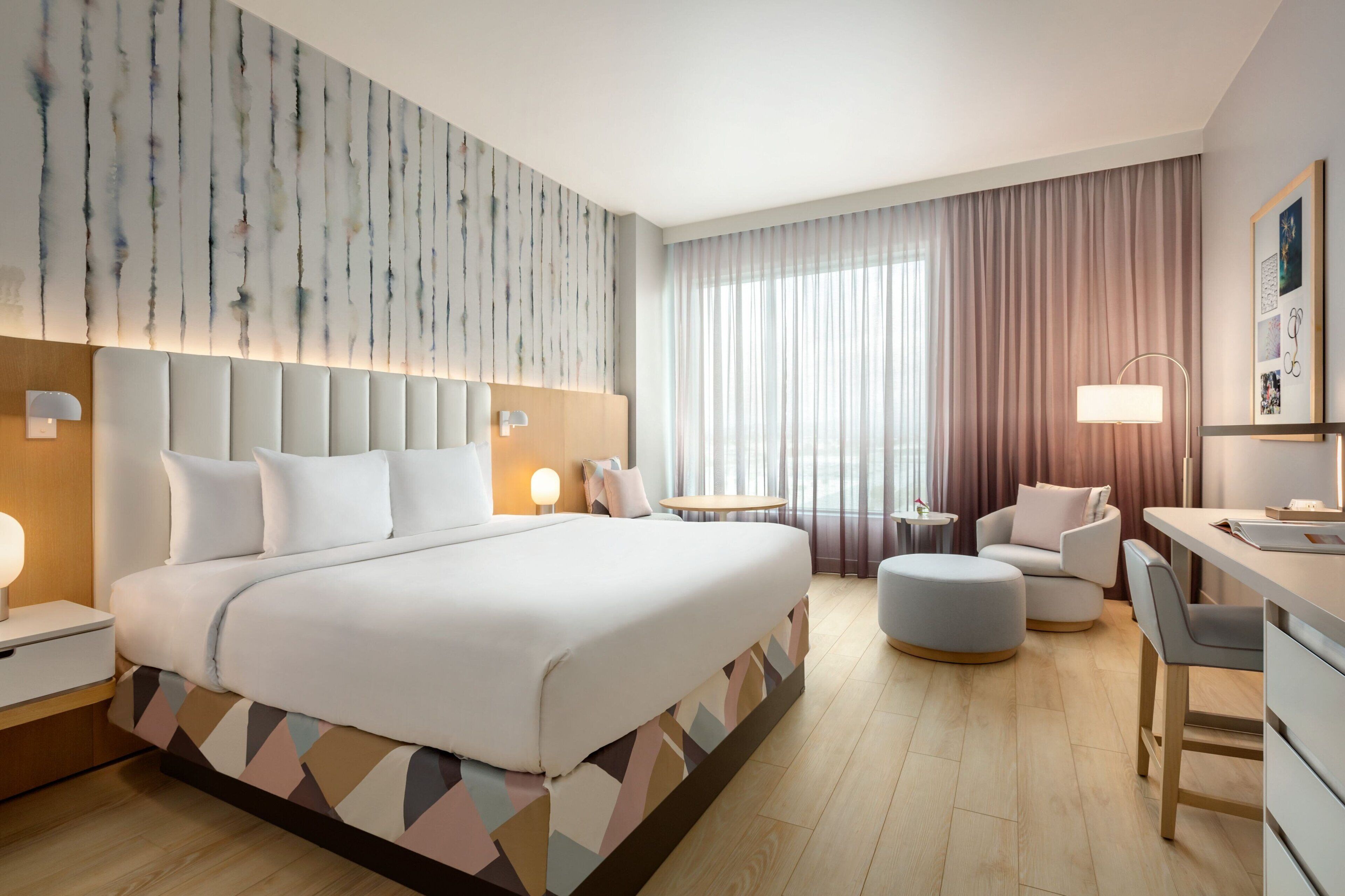 A modern hotel room with a large bed, a desk, a chair, a round table, and a sofa.