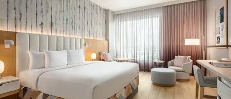A modern hotel room with a large bed, a desk, a chair, a round table, and a sofa.