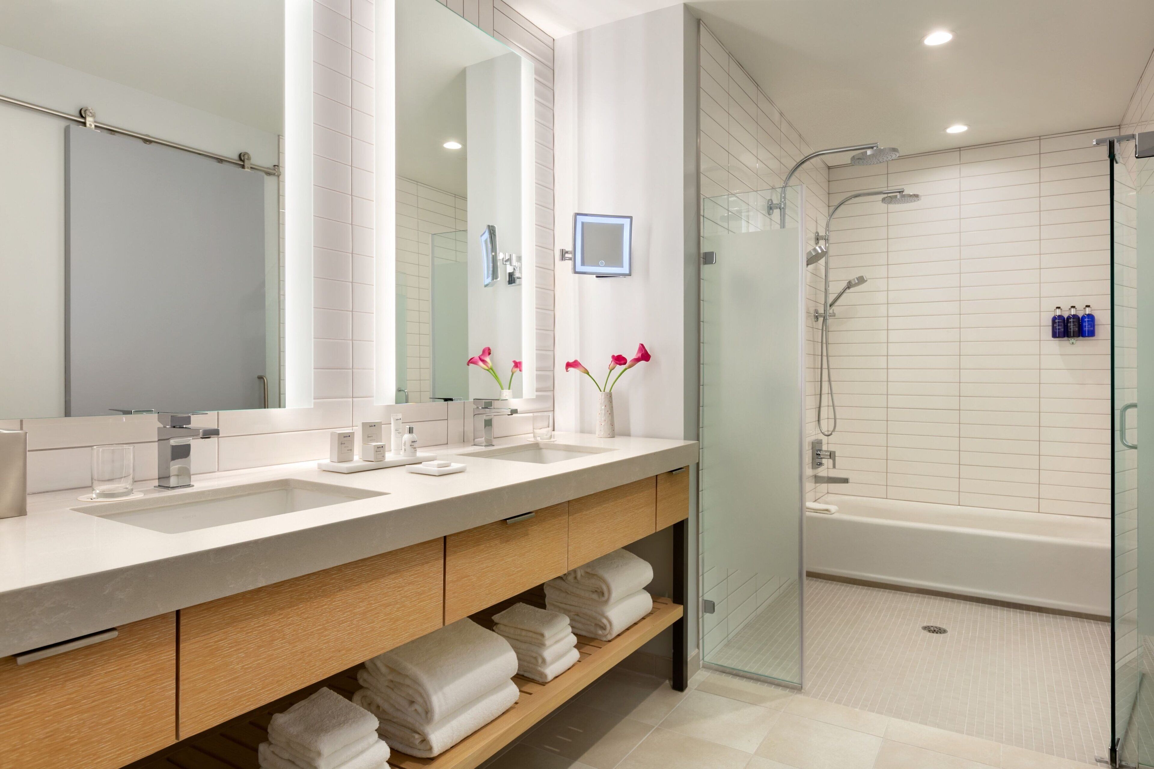 A modern bathroom with two sinks, a large mirror, a glass shower enclosure, and a bathtub.