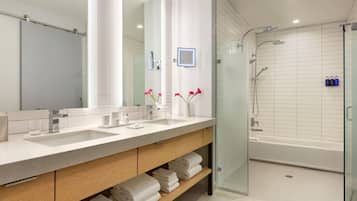 A modern bathroom with two sinks, a large mirror, a glass shower enclosure, and a bathtub.