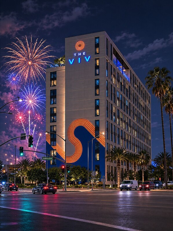 A hotel with a large illuminated 'S' on its facade, located at an intersection with traffic lights and palm trees.