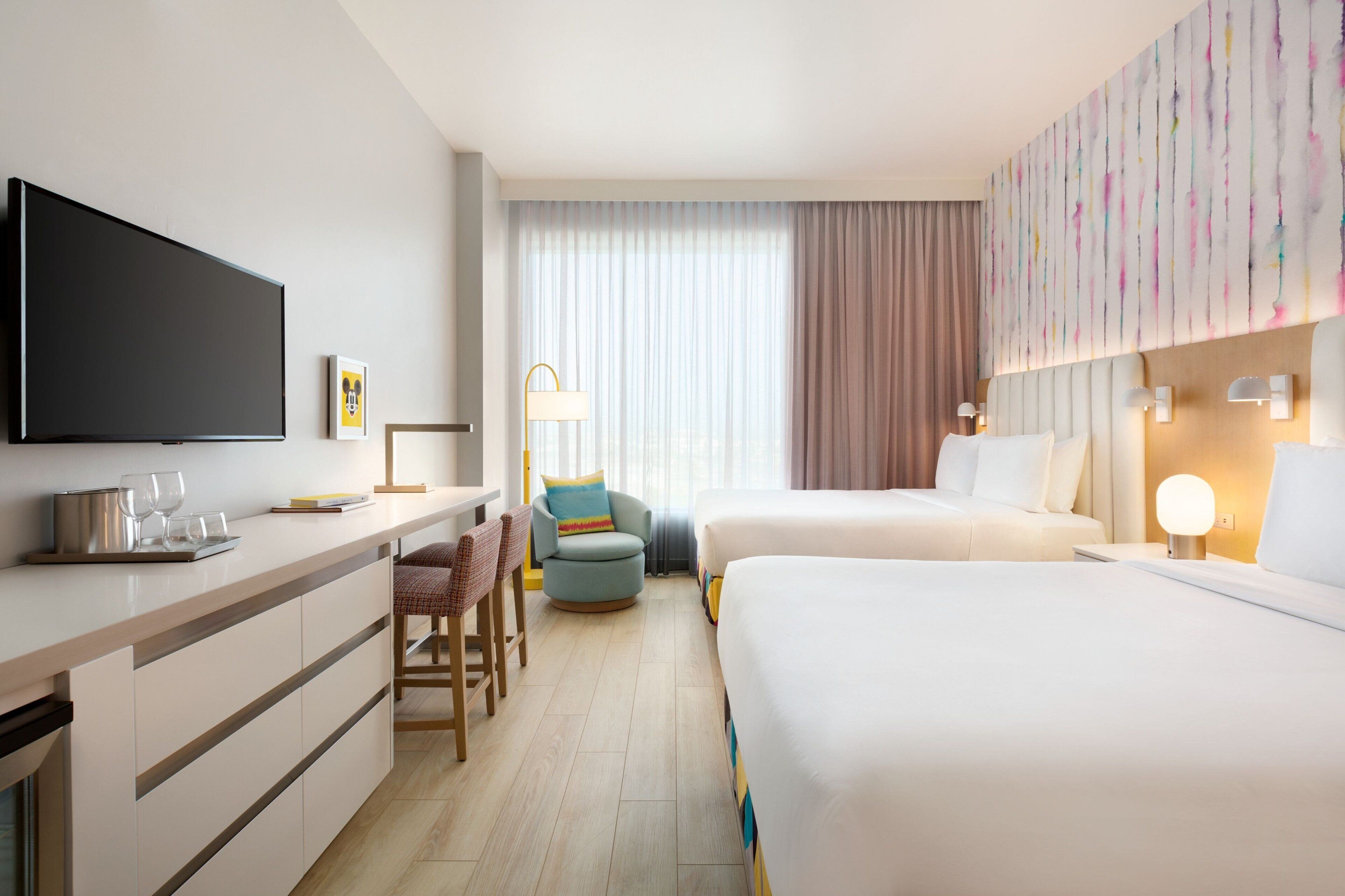 Une chambre d’hôtel équipée d’une télévision à écran plat, d’un bureau avec une chaise, d’un canapé, d’un lit et d’une grande fenêtre avec des rideaux.