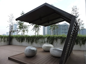 A rooftop garden with a wooden deck, three stone planters, and a metal pergola.