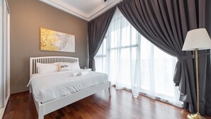 Quarto moderno com cama branca, uma janela ampla com cortinas leves e um abajur.