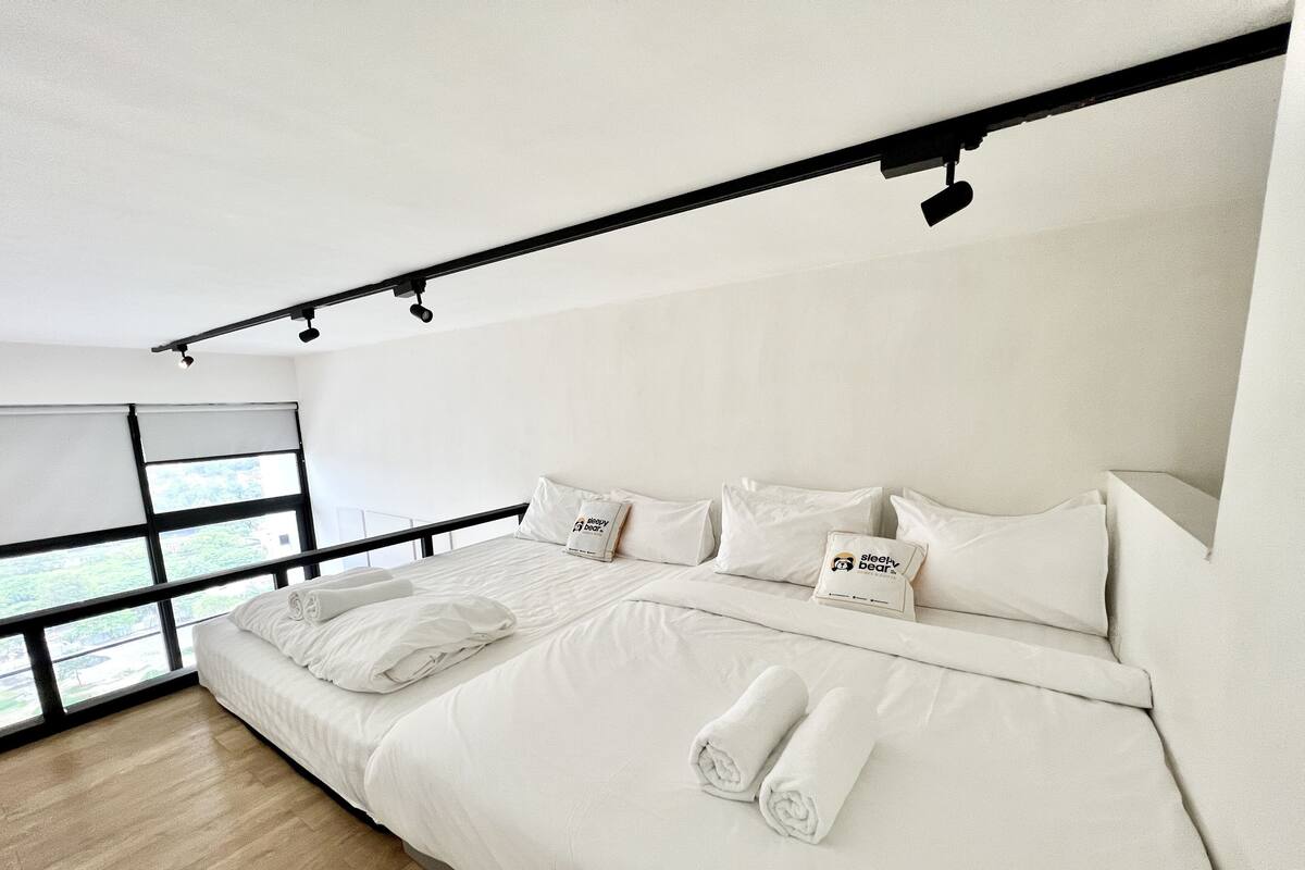 A modern bedroom with a large bed, white bedding, and a view through floor-to-ceiling windows.